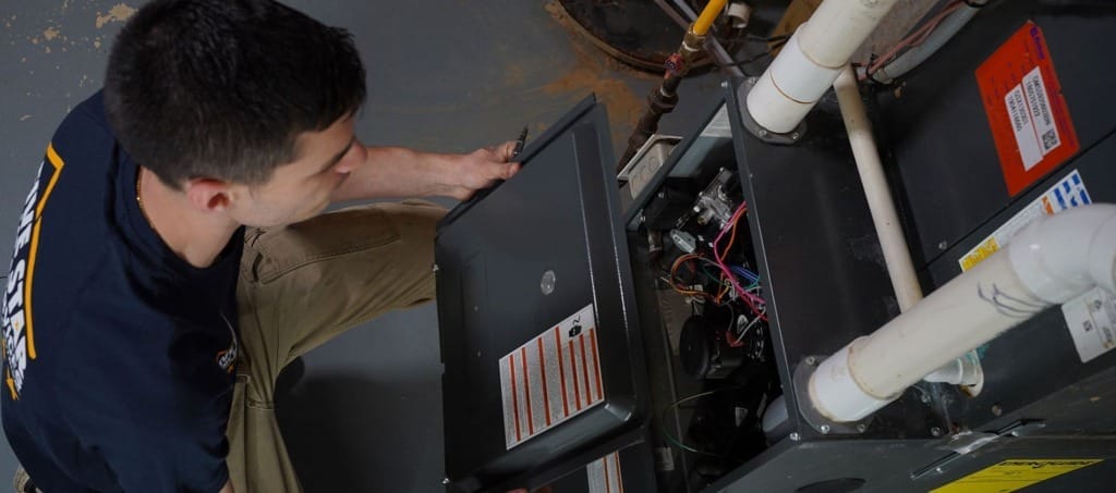 Alt Text: Five Star Home Services technician performing furnace replacement by inspecting and working on the internal components of a residential heating system.